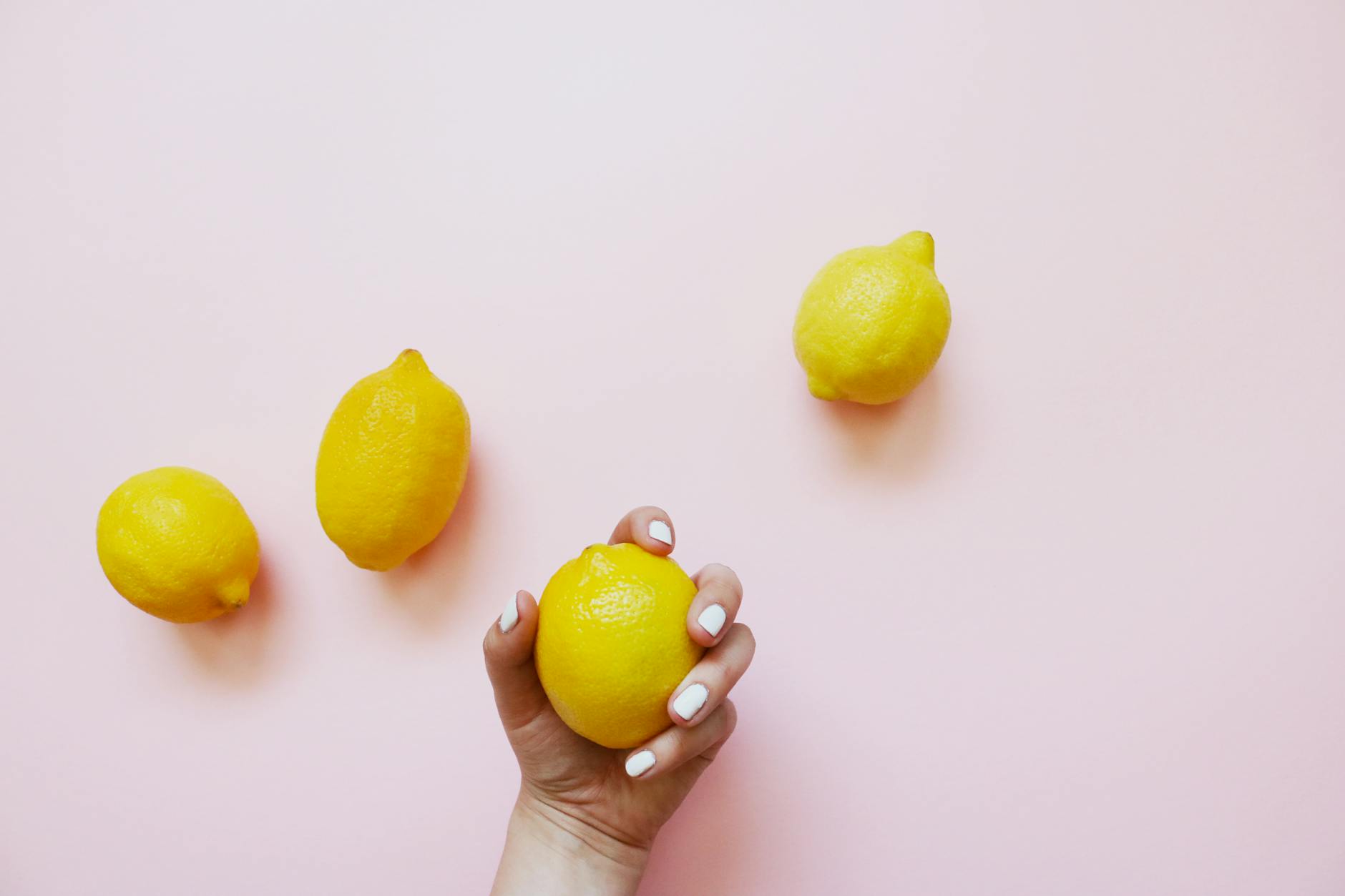 Hand holding a lemon on soft pink background, symbolizing starting fresh with pleasure