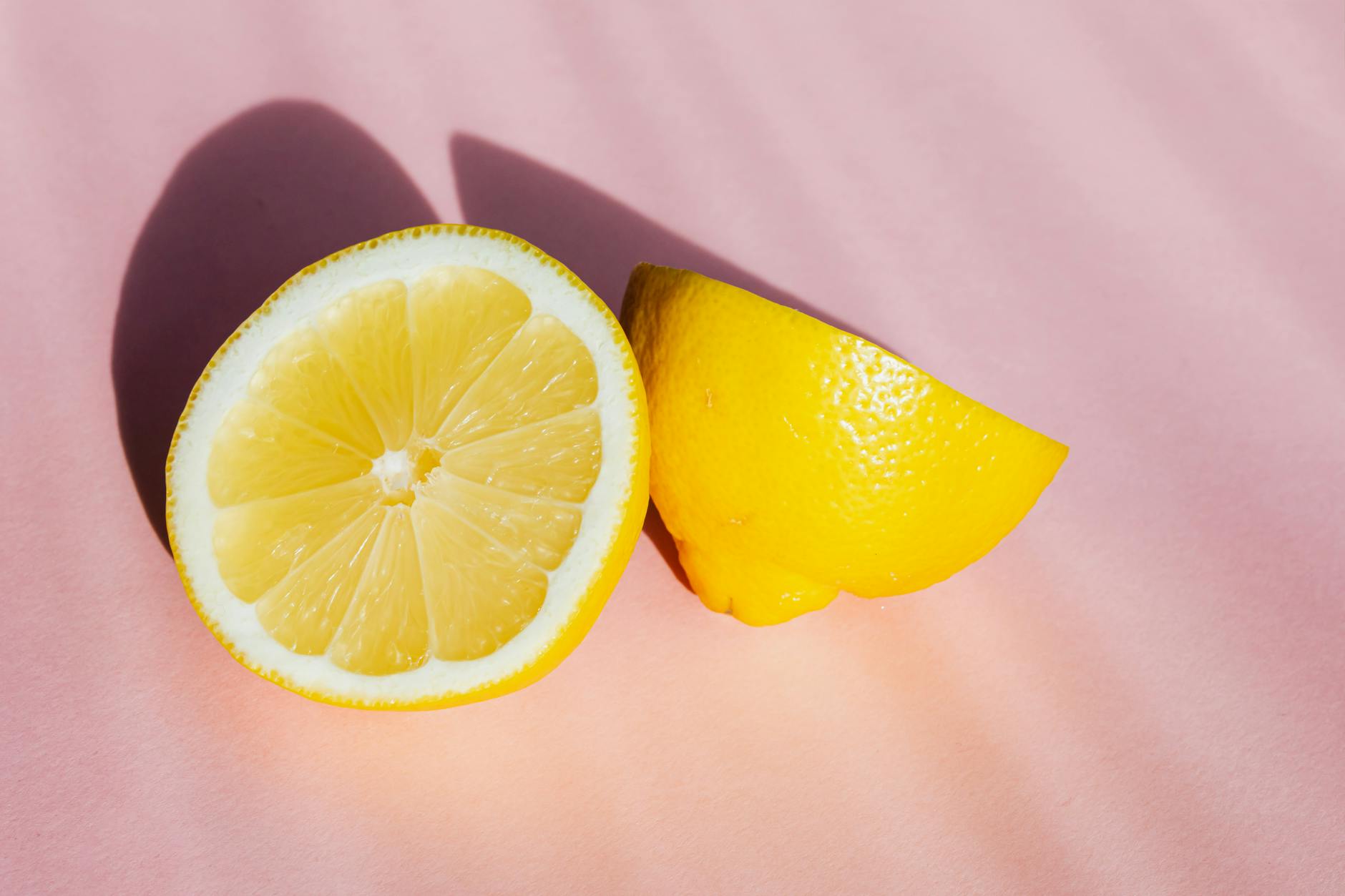 Fresh lemon halves on a pink background, symbolizing the smooth, rounded design of lemon clitoral vibrators