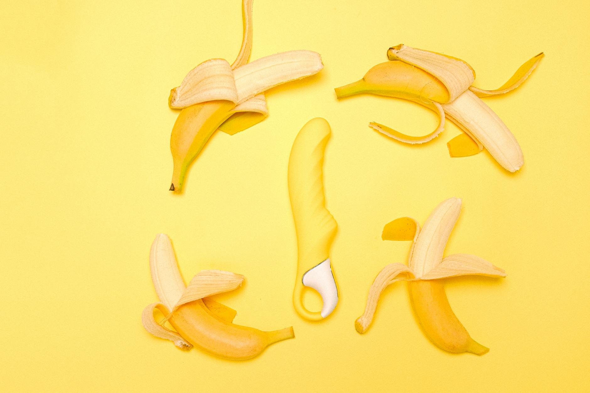Yellow lemon-shaped silicone vibrator surrounded by fresh lemons on bright yellow background