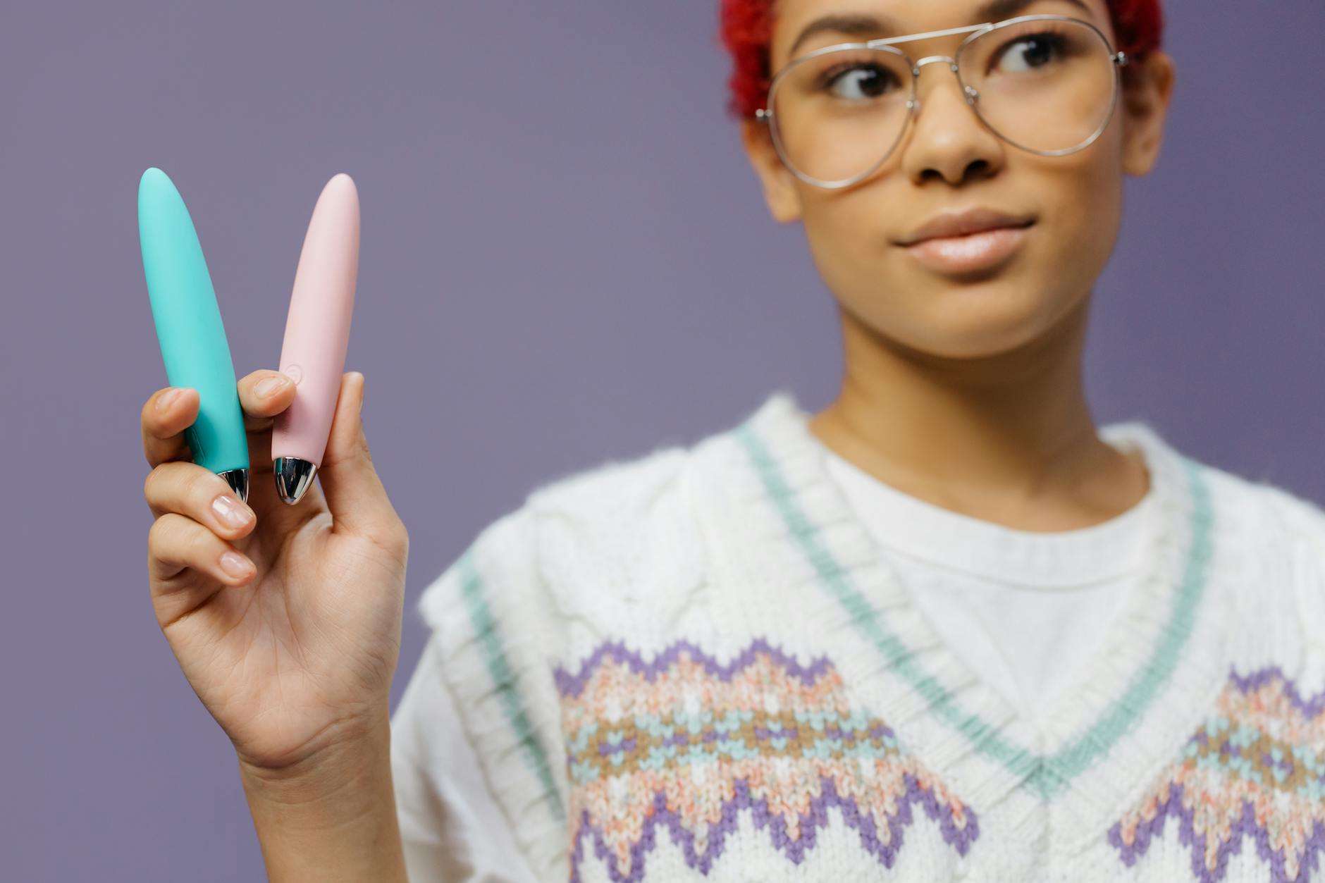 Woman holding two colorful clitoral vibrators including a lemon-shaped device against a purple background