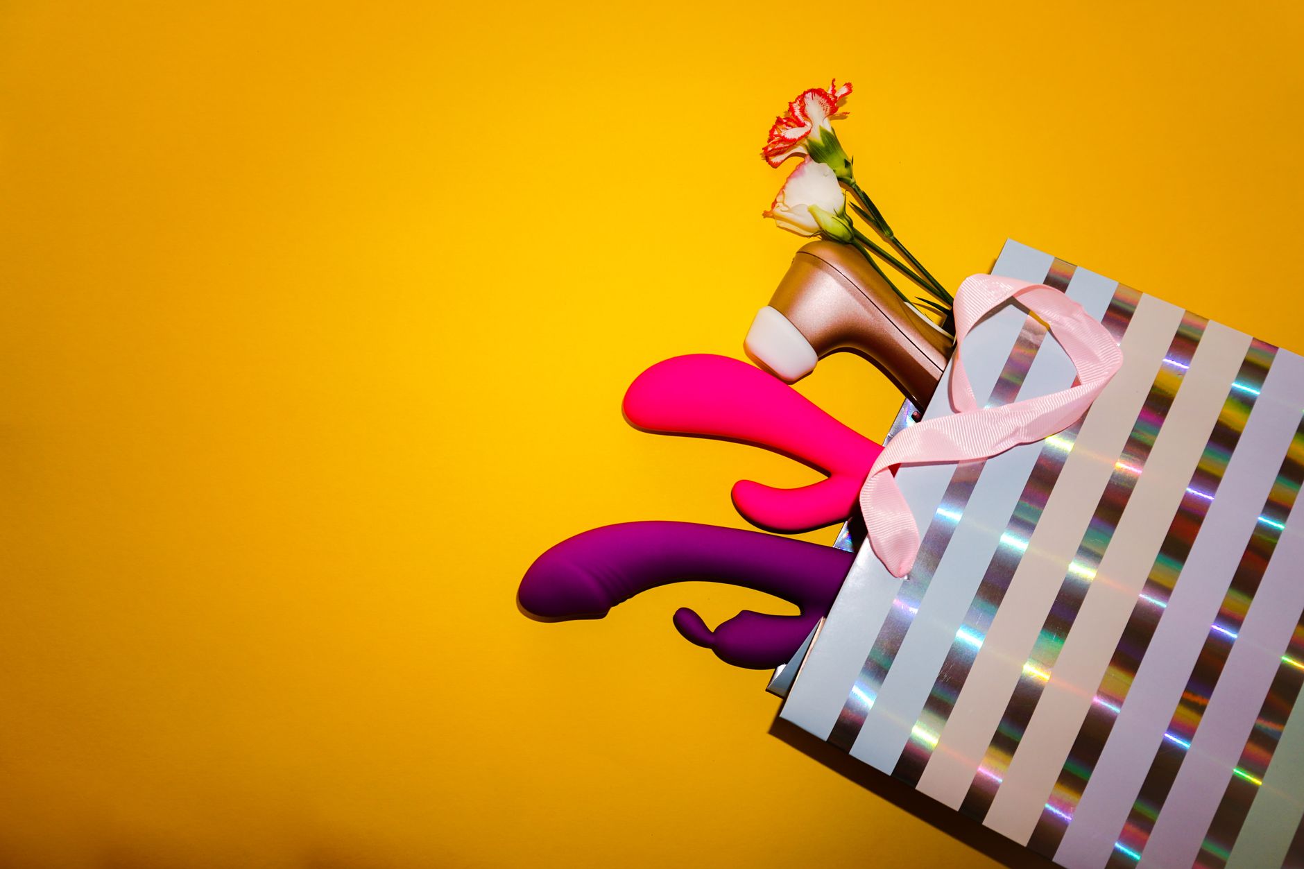 A yellow silicone vibrator surrounded by peeled bananas on a bright yellow background.